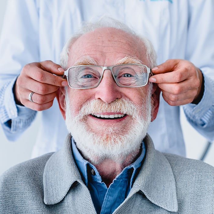Ein alter Mann dem eine Brille angezogen wird
